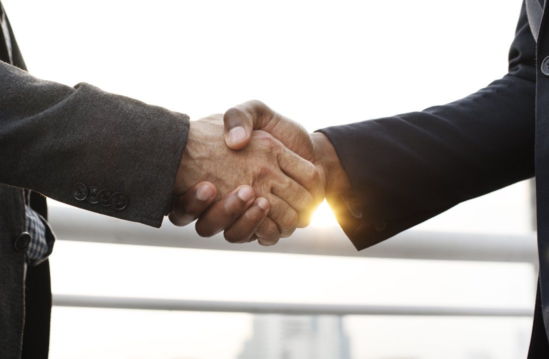 Two businessmen shaking hands in front of a building.