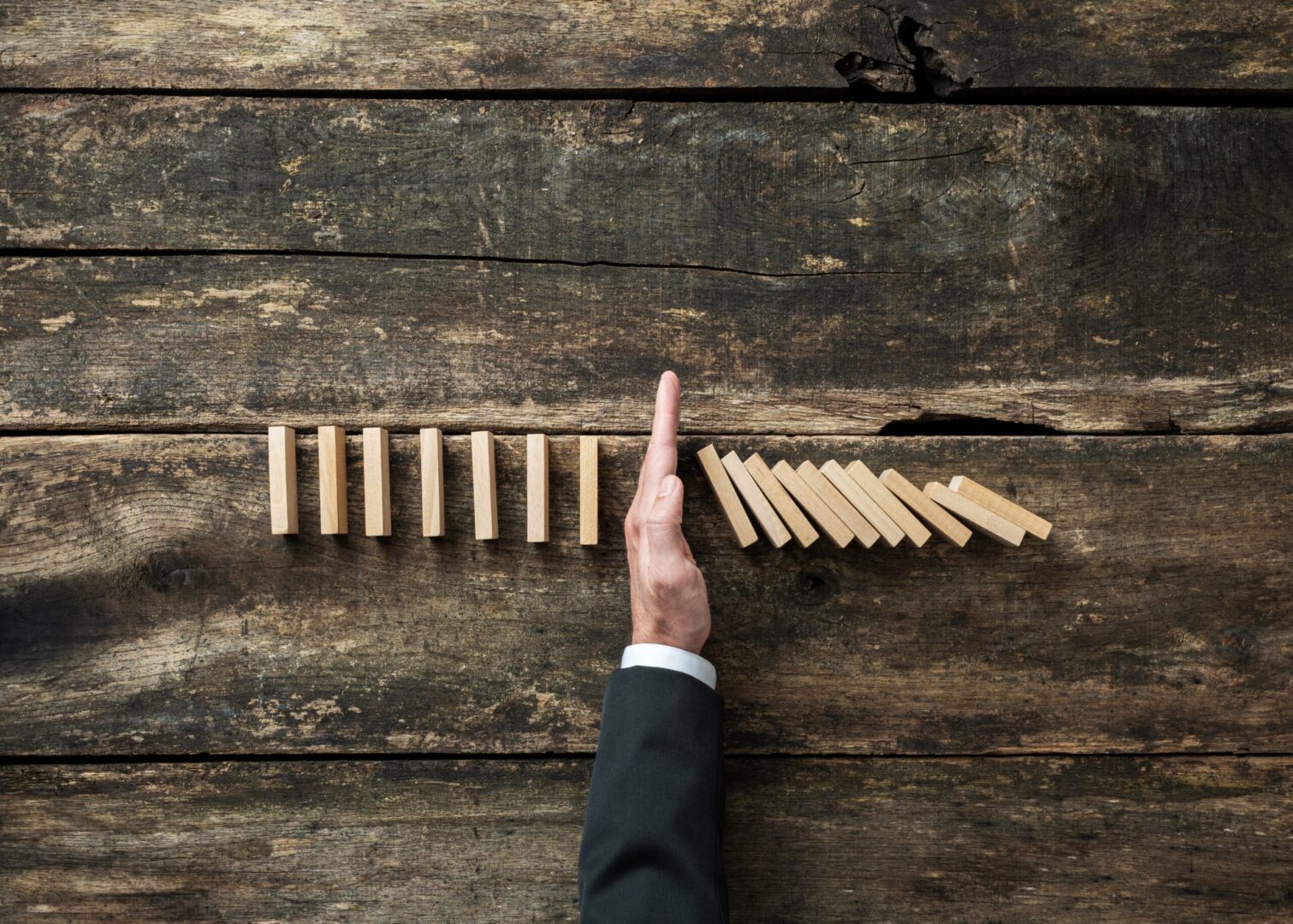 A man in a suit reaching for dominoes on a wooden table.