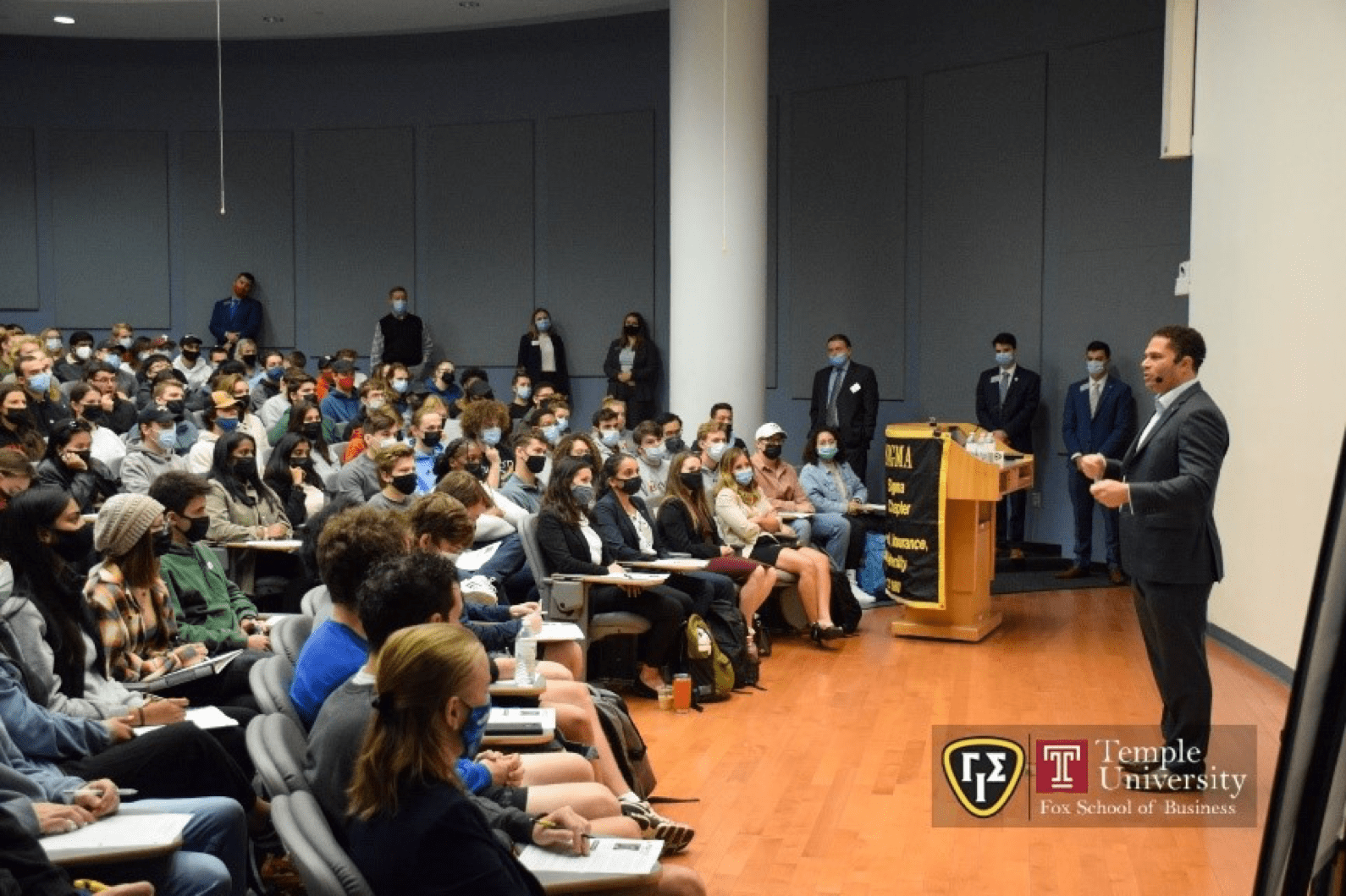 A man in a suit is giving a lecture to a group of people.